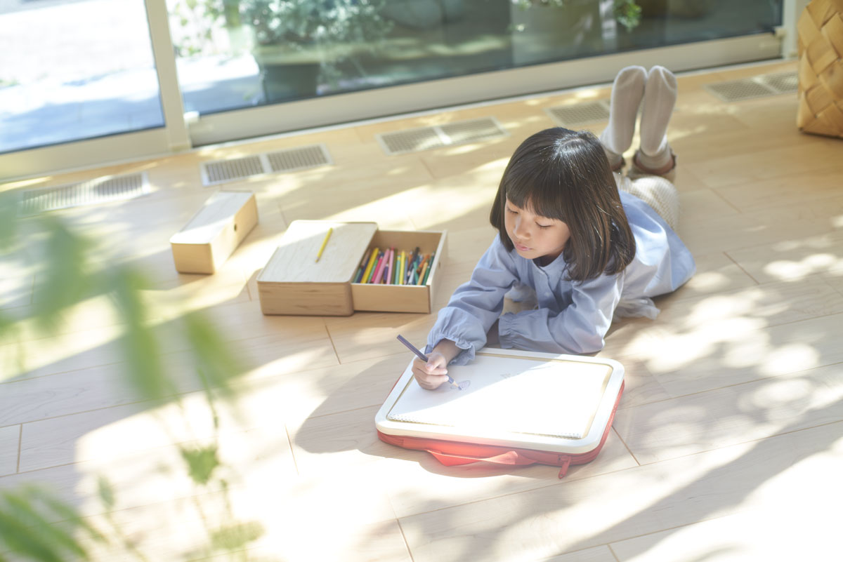 床に寝ころびお絵かきをする女の子