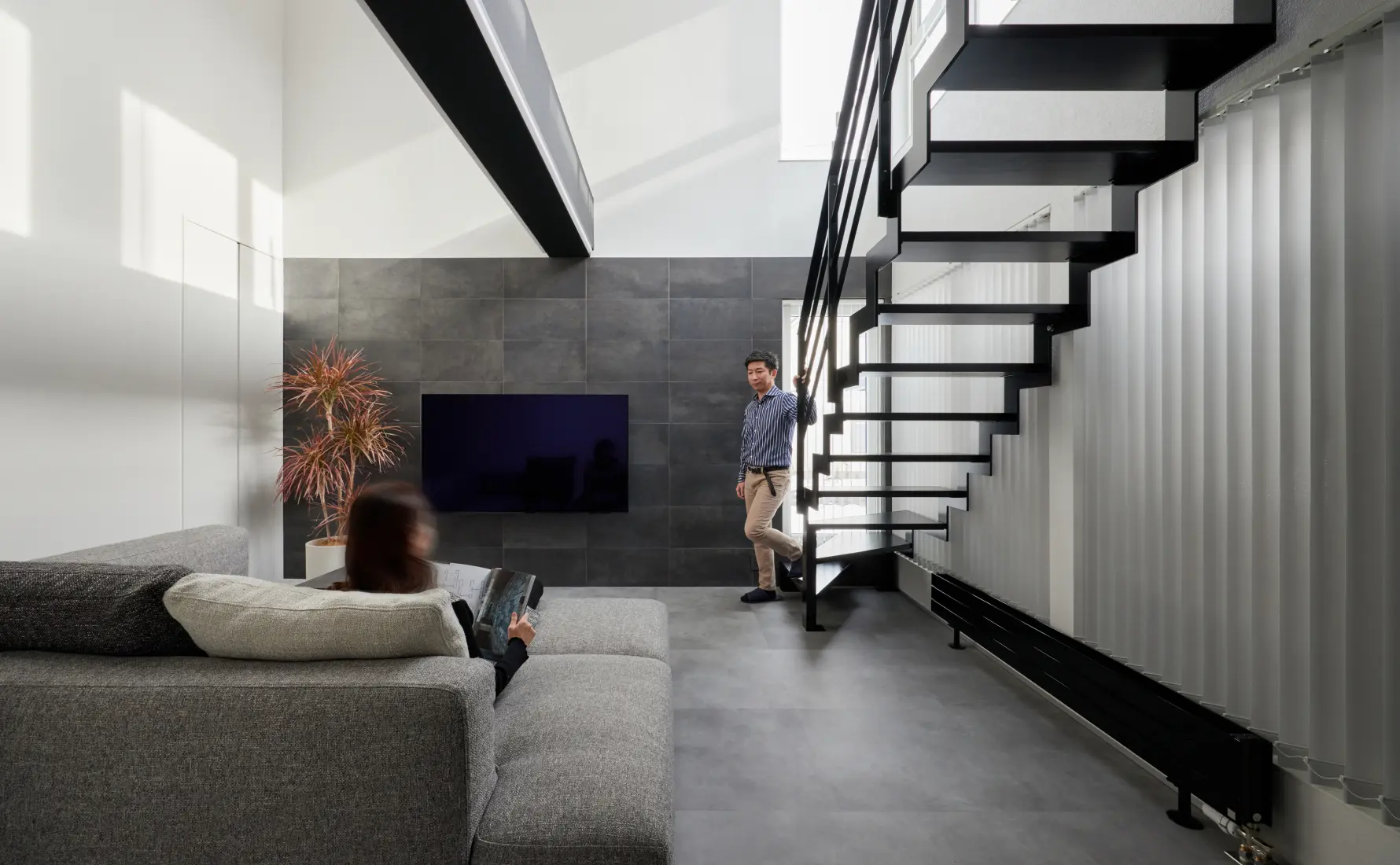 テレビが見える位置のソファに座る奥様と階段横に立つS様