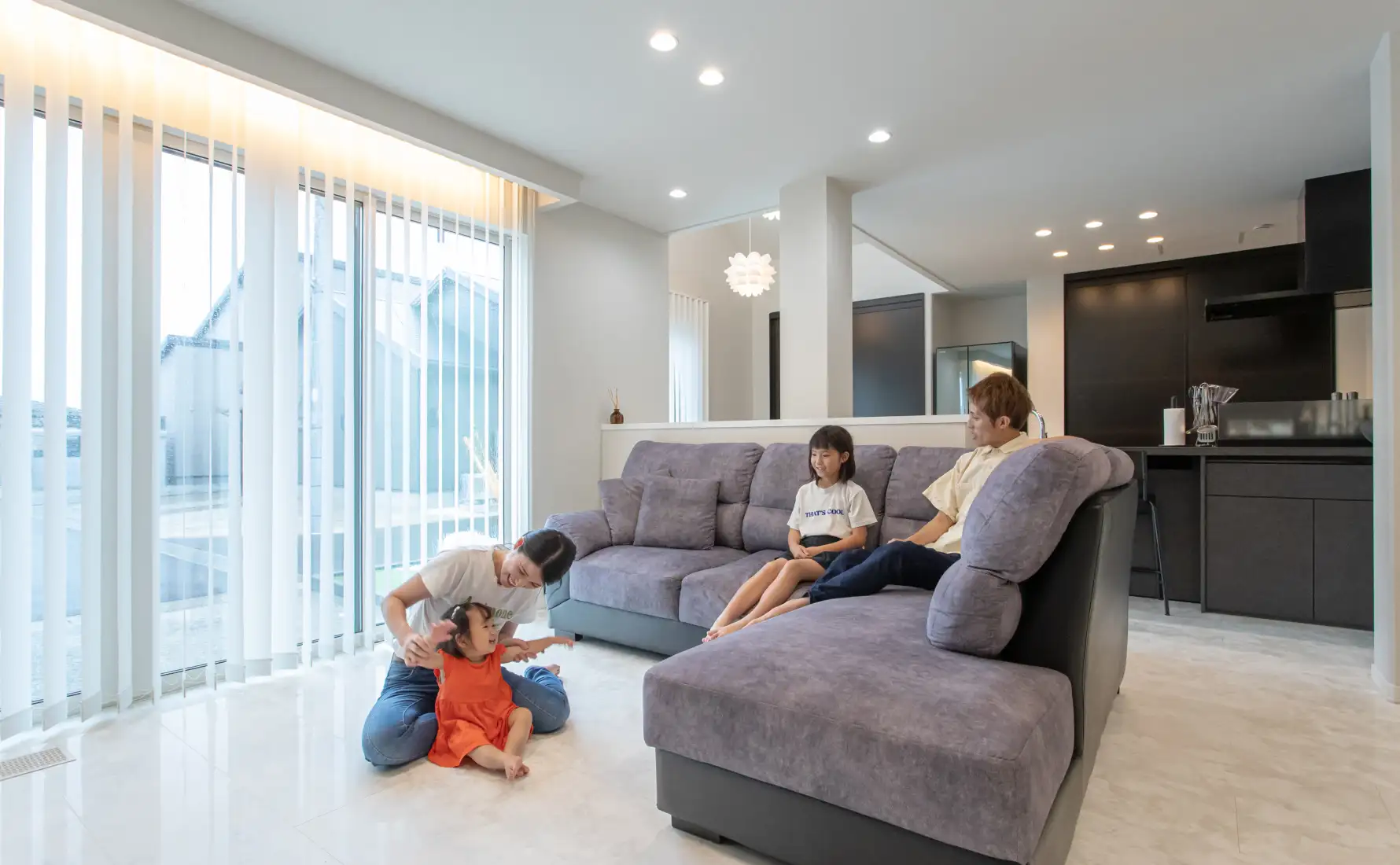 リビングに置かれたL字型ソファに座ったり床で遊んだりする家族