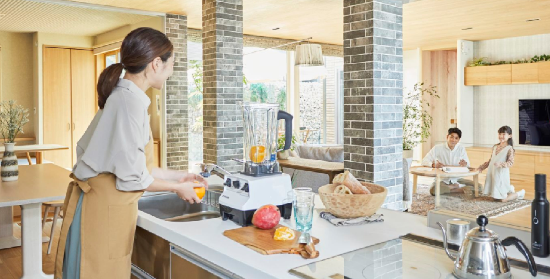 キッチンでジュースをつくる人物と奥のリビングでくつろぐ家族