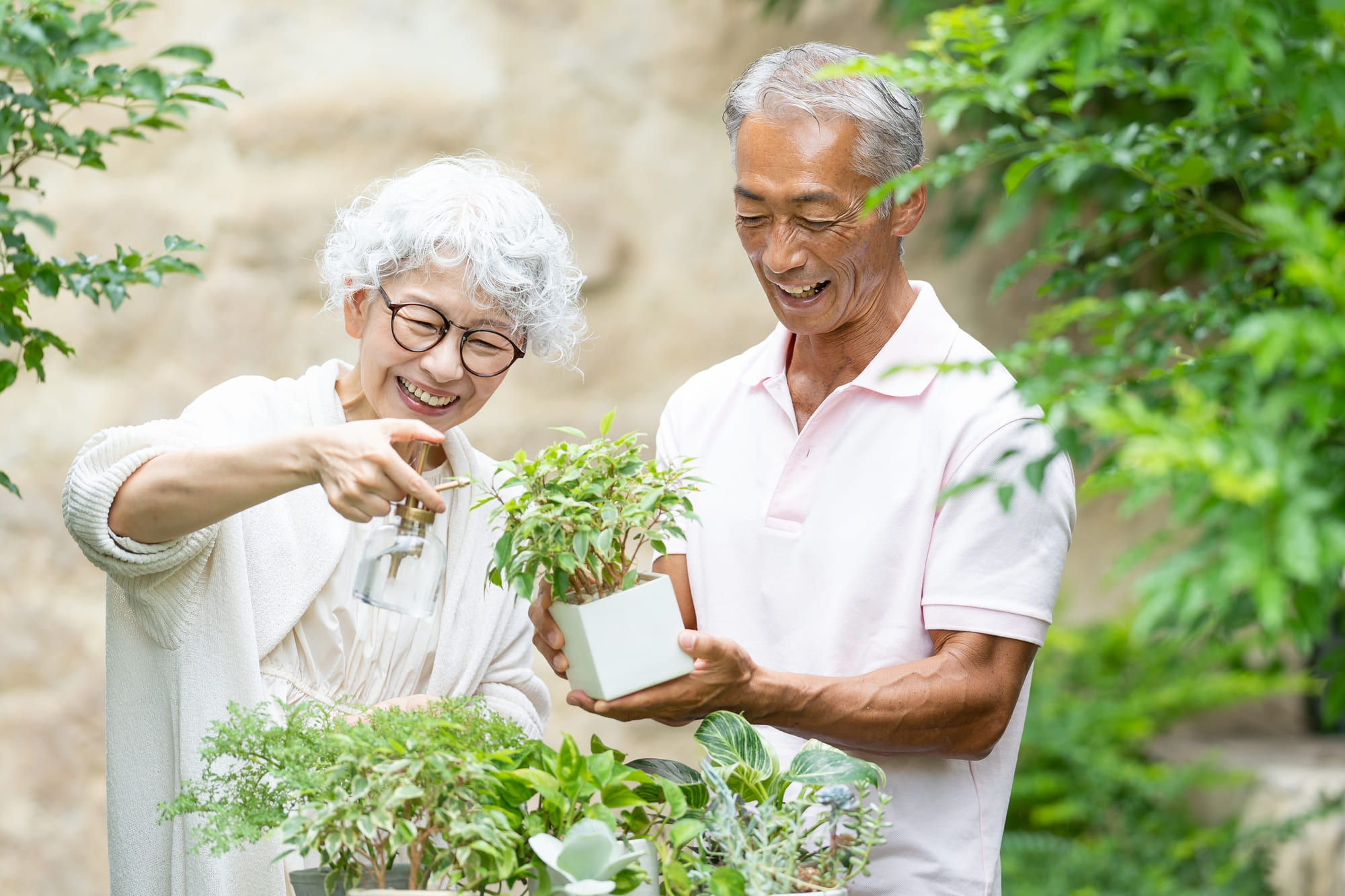 庭で鉢植えに水をあげる高齢の夫婦