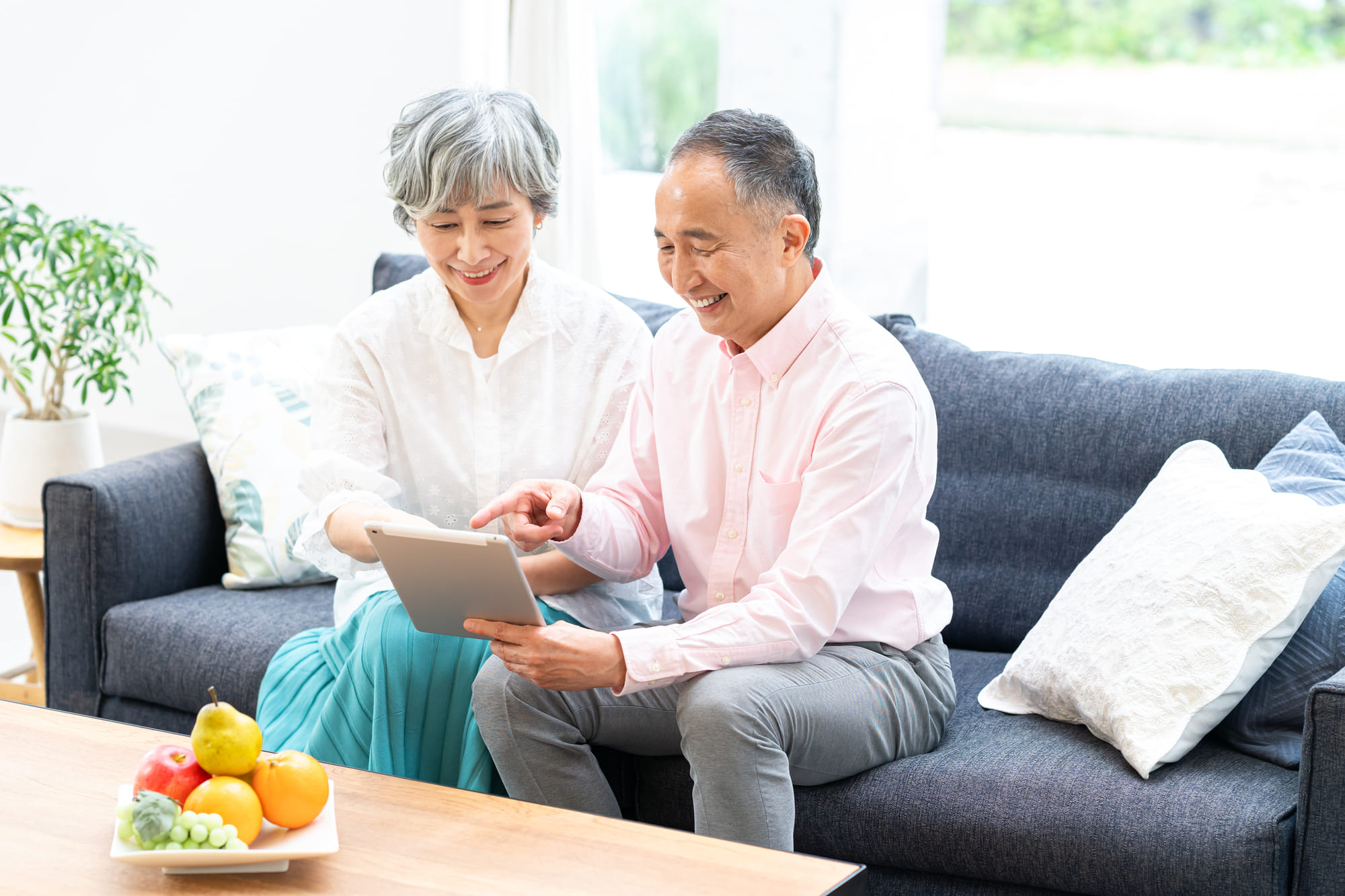 明るいリビングでソファに座ってタブレットを見る高齢夫婦