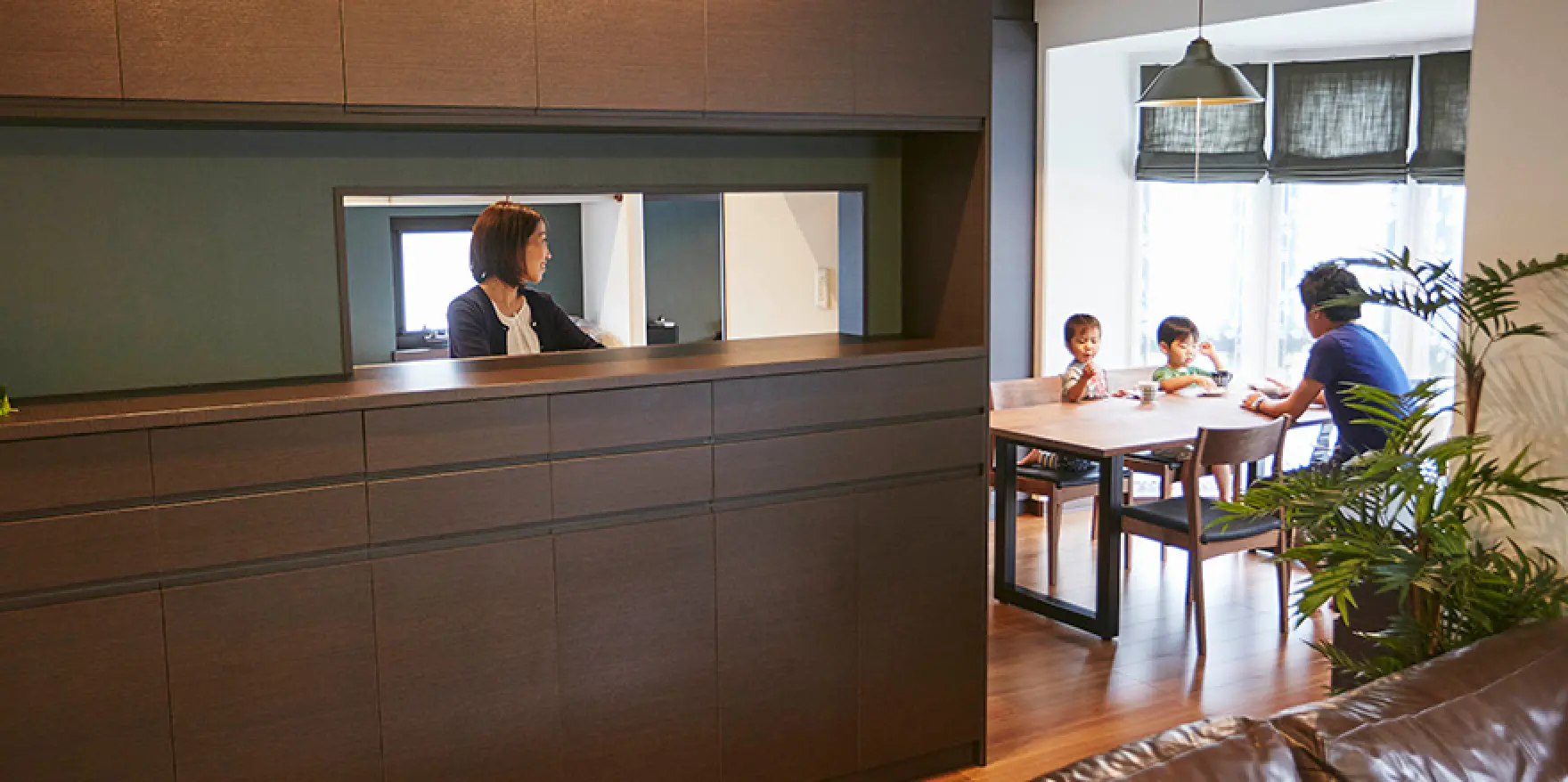 セミオープン型のキッチンから家族を見守る母親とダイニングで食事をとる子供と父親